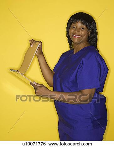Stock Photograph - African-American mid-adult woman in medical uniform smiling reading chart.. Fotosearch