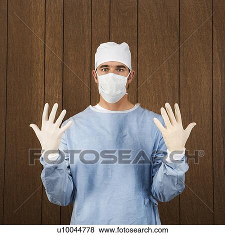 Stock Photo - Caucasian mid-adult male surgeon wearing face mask and holding up gloved hands.. Fotosearch