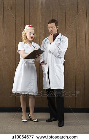 Stock Photo - Mid-adult Caucasian female nurse and male doctor standing looking at clipboard.. Fotosearch