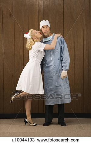 Stock Image - Mid-adult Caucasian female nurse kissing doctor on cheek.. Fotosearch