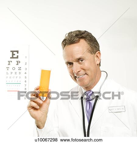 Stock Photo - Mid-adult Caucasian male doctor holding a medical pill bottle with an eye chart in the background.. Fotosearch