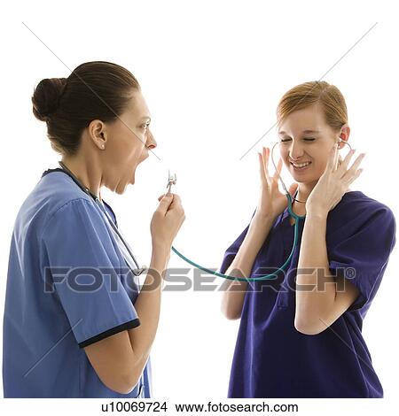 Picture - Portrait of Caucasian healthcare workers wearing scrubs with one yelling into stethoscope that is attached to other's ears against white background.. Fotosearch