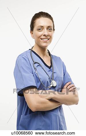Stock Image - Portrait of smiling Caucasian woman doctor standing against white background.. Fotosearch