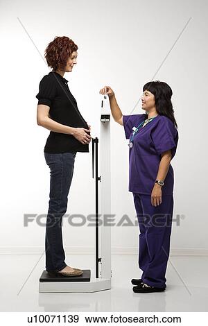 Pregnant Caucasian mid-adult woman being weighed by nurse. View Large Photo Image Stock Photo - Pregnant Caucasian mid-adult woman being weighed by nurse.. Fotosearch