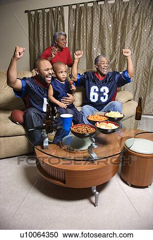 Stock Image - A three generation African-American family cheering and watching football game together on tv. . Fotosearch