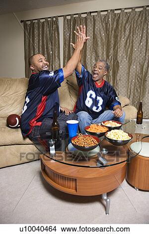 Picture - African-American father and son giving high five while watching football game.. Fotosearch