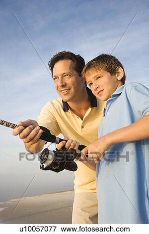 Stock Photo - Caucasian mid-adult man shore fishing on beach with pre-teen boy. Fotosearch
