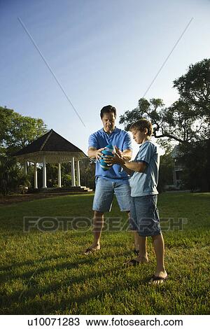 Stock Image - Caucasian mid-adult man teaching football to Caucasian pre-teen boy.. Fotosearch