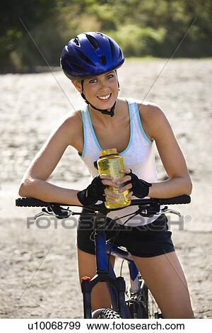 Caucasian mid-adult woman wearing bicycle helmet, sitting on bycycle, holding water bottle, looking at viewer, smiling. View Large Photo Image Stock Photo - Caucasian mid-adult woman wearing bicycle helmet, sitting on bycycle, holding water bottle, looking at viewer, smiling.. Fotosearch