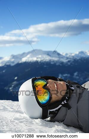 Caucasian teenage boy snowboarder wearing helmet and goggles, smiling, looking at viewer, lying in snow on mountain with mountain landscape in background. View Large Photo Image Stock Photo - Caucasian teenage boy snowboarder wearing helmet and goggles, smiling, looking at viewer, lying in snow on mountain with mountain landscape in background.. Fotosearch