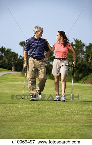 Caucasion mid-adult man and woman walking on golf course talking to each other. View Large Photo Image Stock Photo - Caucasion mid-adult man and woman walking on golf course talking to each other.. Fotosearch