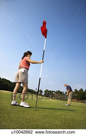 Caucasion mid-adult man putting golfball while Caucasion mid-adult woman holds flag. View Large Photo Image Stock Image - Caucasion mid-adult man putting golfball while Caucasion mid-adult woman holds flag. . Fotosearch