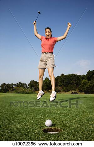 Caucasion mid-adult woman holding golf club jumping in air cheering with golf ball and hole in foreground. View Large Photo Image Stock Photograph - Caucasion mid-adult woman holding golf club jumping in air cheering with golf ball and hole in foreground.. Fotosearch