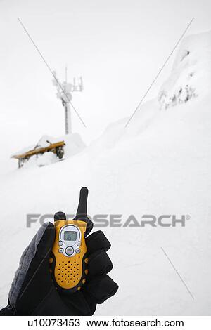 Stock Image - Gloved hand holding walkie talkie in snow scene.. Fotosearch