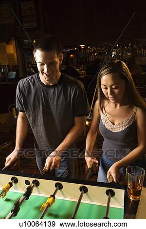 Stock Photo - Young couple teamed up at foosball game in pub.. Fotosearch