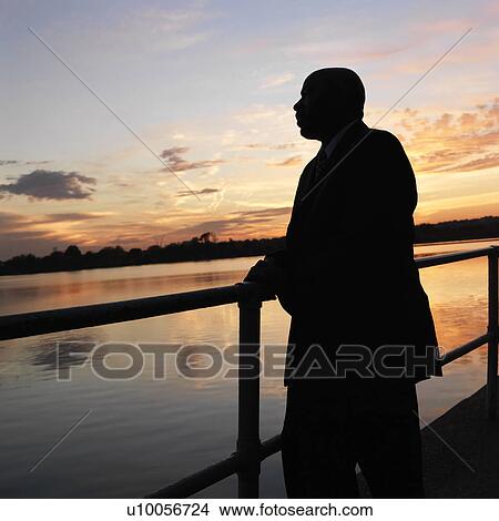 Picture - African-American man standing by water at sunset in Washington, D. C., USA.. Fotosearch
