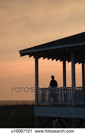 Boy on beachfront porch silhouetted at sunset View Large Photo Image Stock Image - Boy on beachfront porch silhouetted at sunset. Fotosearch