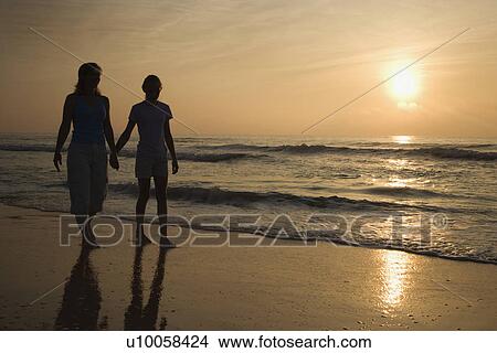Caucasian prime adult female and female child walking on beach at sunset holding hands. View Large Photo Image Picture - Caucasian prime adult female and female child walking on beach at sunset holding hands.. Fotosearch