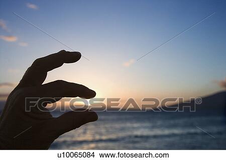 Hand in foreground with fingers around sunrise over the coast of Kihei, Maui, Hawaii, USA. View Large Photo Image Picture - Hand in foreground with fingers around sunrise over the coast of Kihei, Maui, Hawaii, USA.. Fotosearch