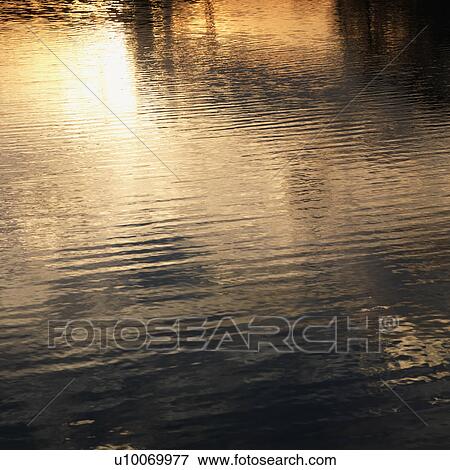 Stock Photo - Reflections of orange and yellow sunset on water.. Fotosearch