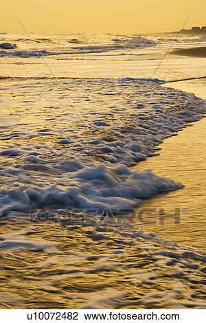 Stock Image - Waves lapping on beach at sunset.. Fotosearch