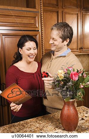 Stock Image - Caucasian man giving Caucasian woman card, present and flowers.. Fotosearch
