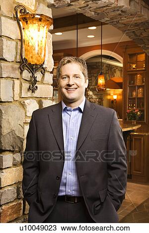 Stock Image - Caucasian man standing with hands in pockets looking at viewer and smiling.. Fotosearch