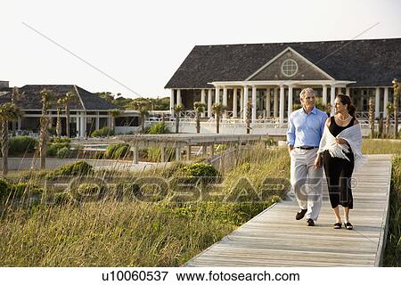 Caucasian mid-adult couple walking on walkway near beach home. View Large Photo Image Stock Photo - Caucasian mid-adult couple walking on walkway near beach home.. Fotosearch