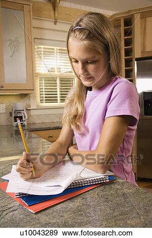 Stock Photo - Caucasian pre-teen girl doing homework at kitchen counter.. Fotosearch