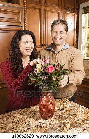 Stock Photo - Caucasian woman and man smiling and arranging flowers together in kitchen.. Fotosearch