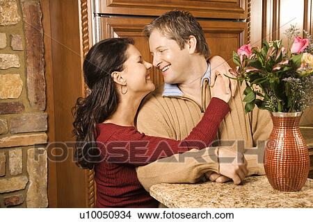 Caucasian woman with arms around Caucasian man smiling at each other in kitchen. View Large Photo Image Picture - Caucasian woman with arms around Caucasian man smiling at each other in kitchen.. Fotosearch
