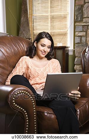 Caucasian/Hispanic young woman sitting in leather chair looking at laptop computer. View Large Photo Image Stock Image - Caucasian/Hispanic young woman sitting in leather chair looking at laptop computer.. Fotosearch
