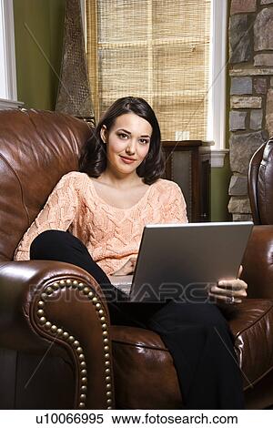 Caucasian/Hispanic young woman sitting in leather chair with laptop looking at viewer. View Large Photo Image Stock Photography - Caucasian/Hispanic young woman sitting in leather chair with laptop looking at viewer.. Fotosearch