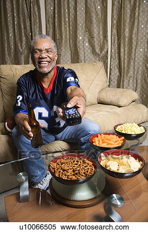 Portrait of a Middle-aged African-American man wearing a football jersey surrounded by snacks pointing a remote at viewer. View Large Photo Image Stock Photography - Portrait of a Middle-aged African-American man wearing a football jersey surrounded by snacks pointing a remote at viewer.. Fotosearch