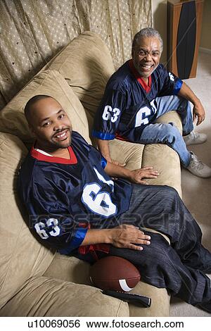 Portrait of an African-American father and son sitting on couch smiling and wearing football jerseys. View Large Photo Image Stock Photograph - Portrait of an African-American father and son sitting on couch smiling and wearing football jerseys.. Fotosearch