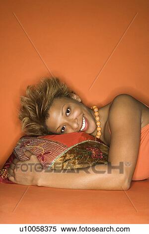 Portrait of smiling African-American young adult woman on orange background lying on floor with head on decorative pillow. View Large Photo Image Stock Photography - Portrait of smiling African-American young adult woman on orange background lying on floor with head on decorative pillow.. Fotosearch