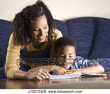 Stock Photograph - Portrait of young boy doing homework while mother looks over shouulder.. Fotosearch