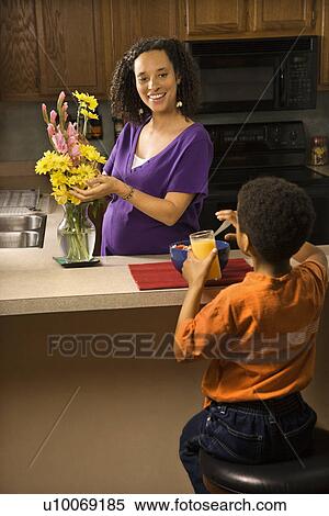 Portrait of young pregnant mother arranging flowers while son eats breakfast. View Large Photo Image Stock Photography - Portrait of young pregnant mother arranging flowers while son eats breakfast. . Fotosearch