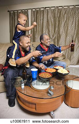 Stock Image - Three male generations of an African-American family watching football game on tv.. Fotosearch