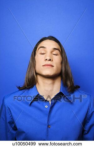 Stock Photo - Portrait of Asian-American teen boy with eyes closed against blue background.. Fotosearch
