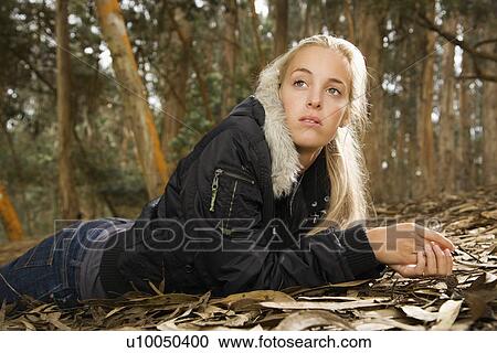 Stock Image - Young adult Caucasian woman lying on ground in forest.. Fotosearch