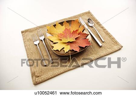 Stock Image - Table setting with plate full of multicolor leaves as main meal.. Fotosearch