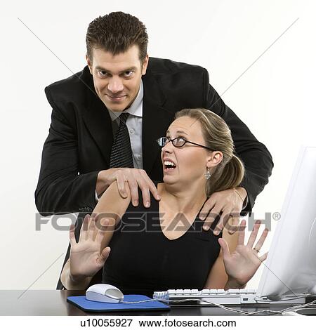 Stock Photo - Caucasian mid-adult man sexually harassing woman sitting at computer and looking at viewer.. Fotosearch
