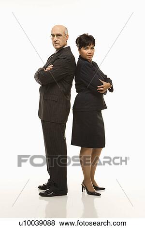 Stock Photo - Caucasian middle-aged businessman and Filipino businesswoman standing back to back with arms crossed looking serious.. Fotosearch