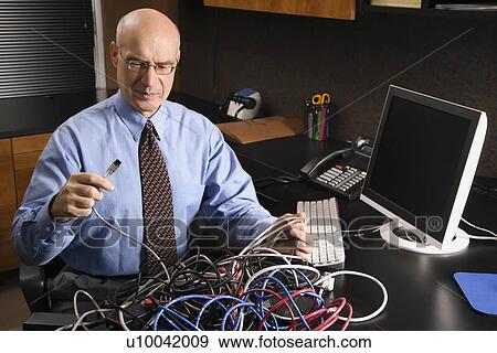 Stock Photo - Caucasian middle-aged businessman at desk in office with a tangle of computer cables.. Fotosearch