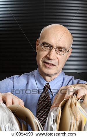 Stock Image - Caucasian middle-aged businessman looking through files.. Fotosearch