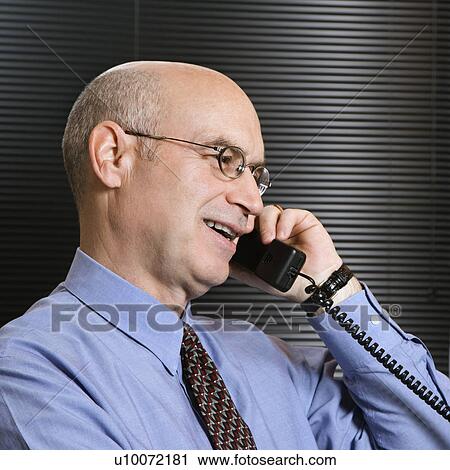 Stock Image - Caucasian middle-aged businessman smiling and talking on telephone.. Fotosearch