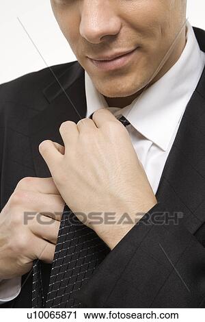 Stock Image - Close-up of Claucasian mid-adult man straightening necktie.. Fotosearch