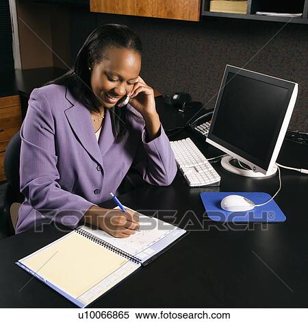 High angle view of African-American young adult business woman talking on cell phone and writing in planner in office. View Large Photo Image Stock Photography - High angle view of African-American young adult business woman talking on cell phone and writing in planner in office.. Fotosearch