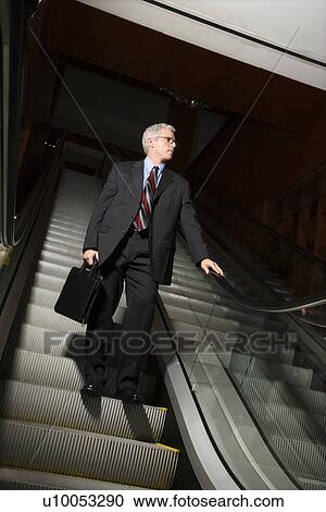 Prime adult Caucasian man in suit holding briefcase standing on down escalator holding rail. View Large Photo Image Stock Image - Prime adult Caucasian man in suit holding briefcase standing on down escalator holding rail.. Fotosearch